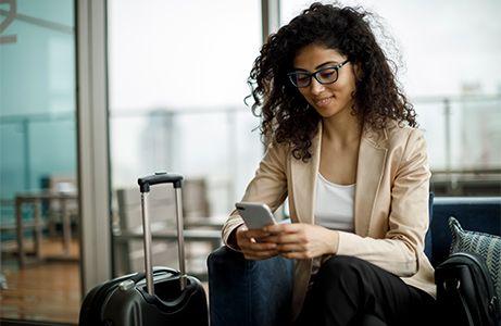 Corporate traveler looking at phone with carry on bag